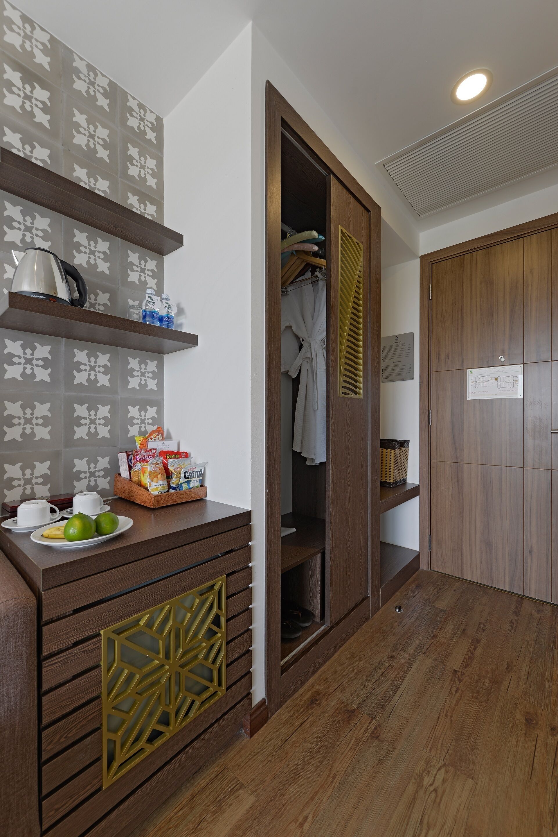 A hotel room with a wooden cabinet, a tray with snacks, a white towel, and a wooden door.