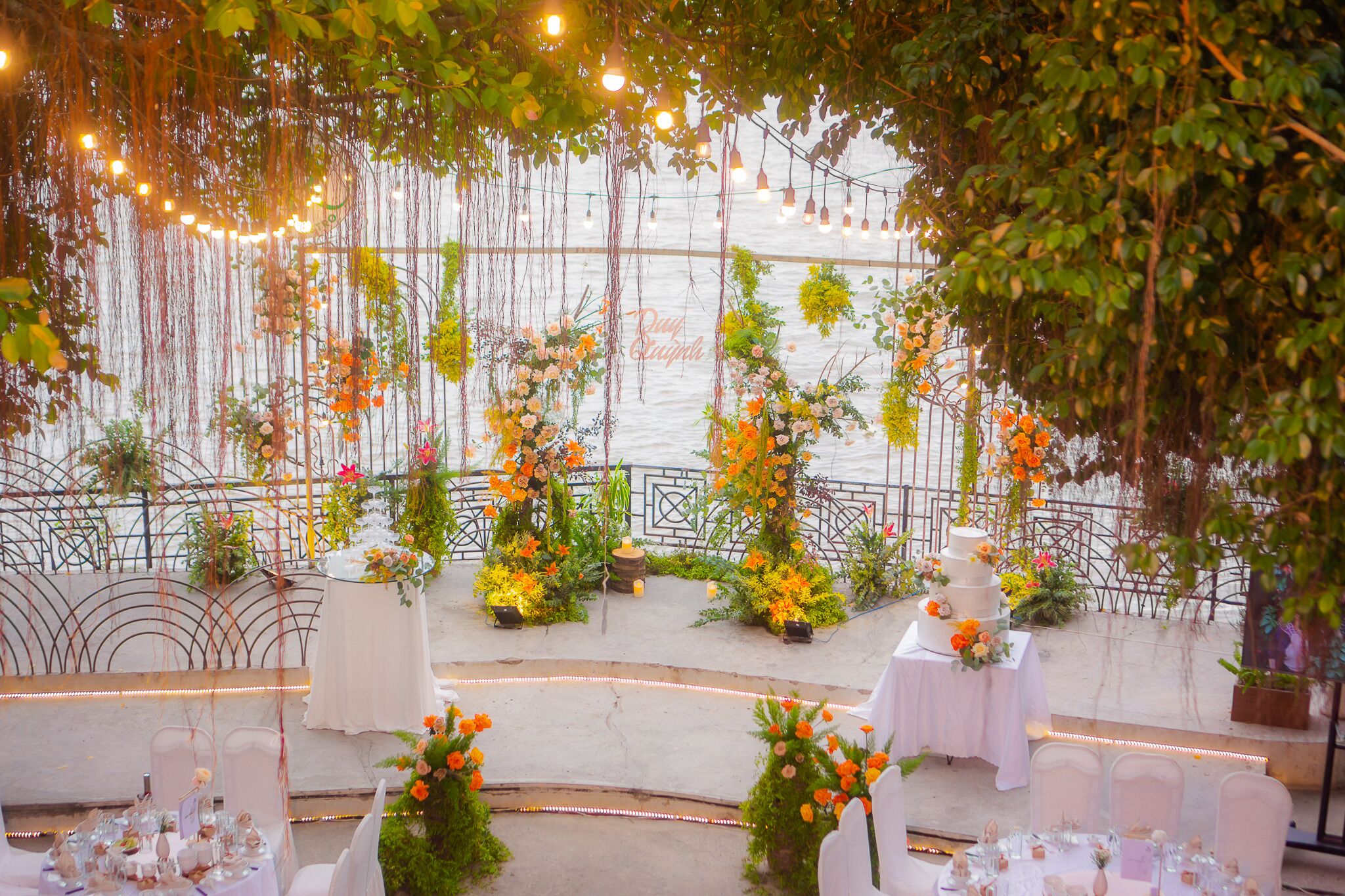 Salón de bodas al aire libre con mesas dispuestas para los invitados, rodeado de follaje y arreglos florales.