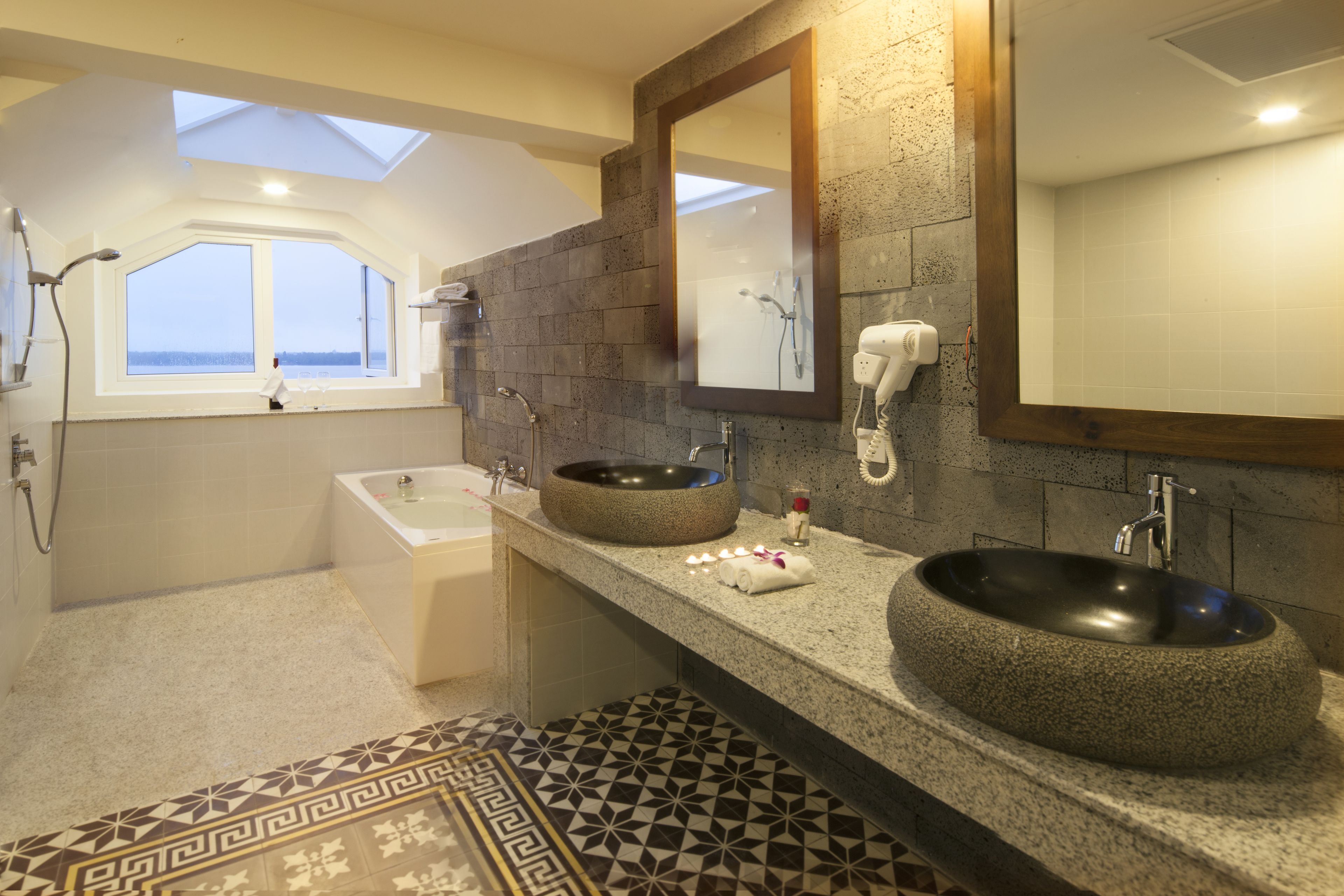 A modern bathroom with a skylight, a large round sink, a bathtub, and a vanity with a mirror.
