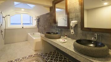 A modern bathroom with a skylight, a large round sink, a bathtub, and a vanity with a mirror.