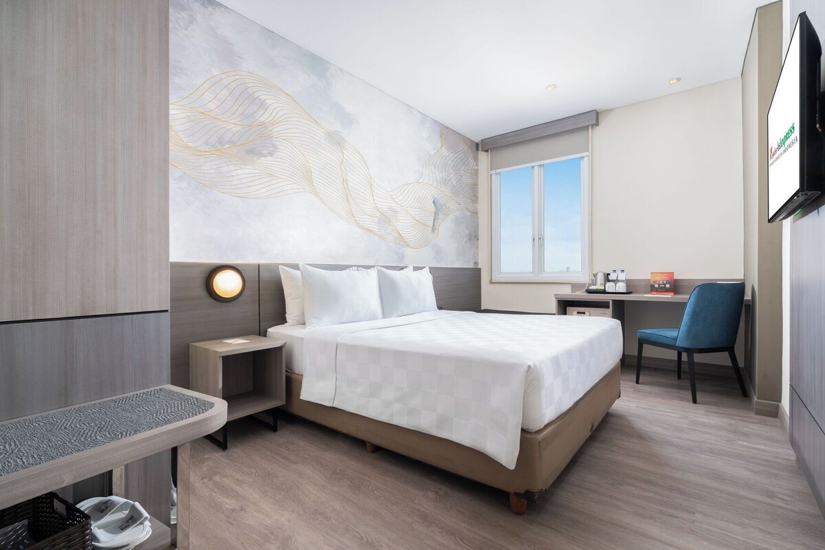 A hotel room with a bed, bedside table, chair, desk, and a large abstract wall mural.