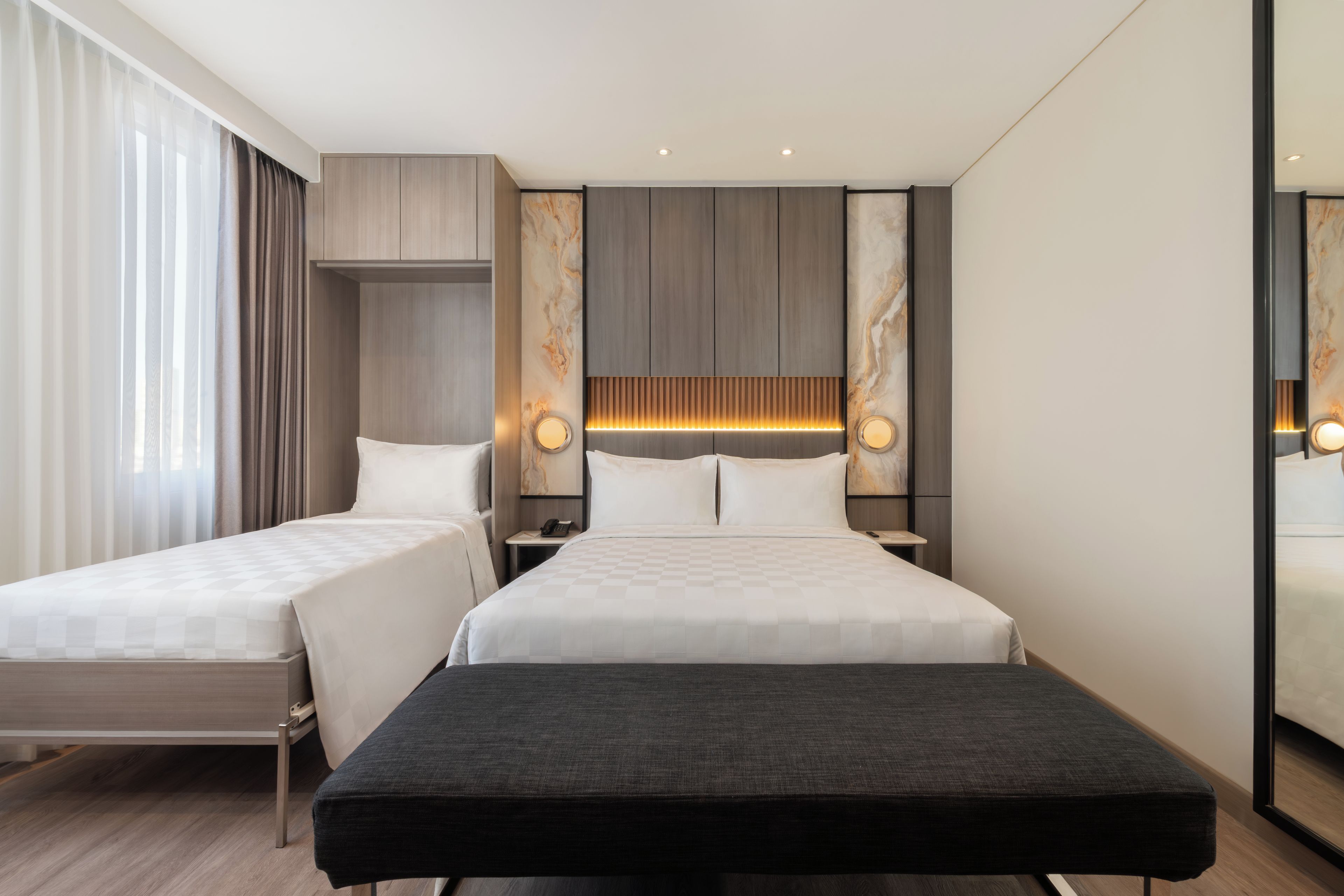 Ein Hotelzimmer mit zwei Betten, einer Bank, einem Nachttisch mit Telefon und einer Wand mit Marmoroptik.