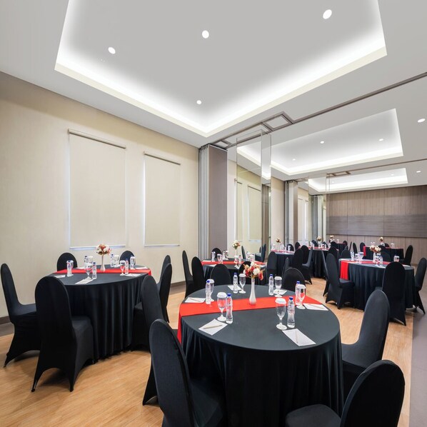 Une salle de conférence avec des tables rondes, des chaises noires et une nappe rouge.