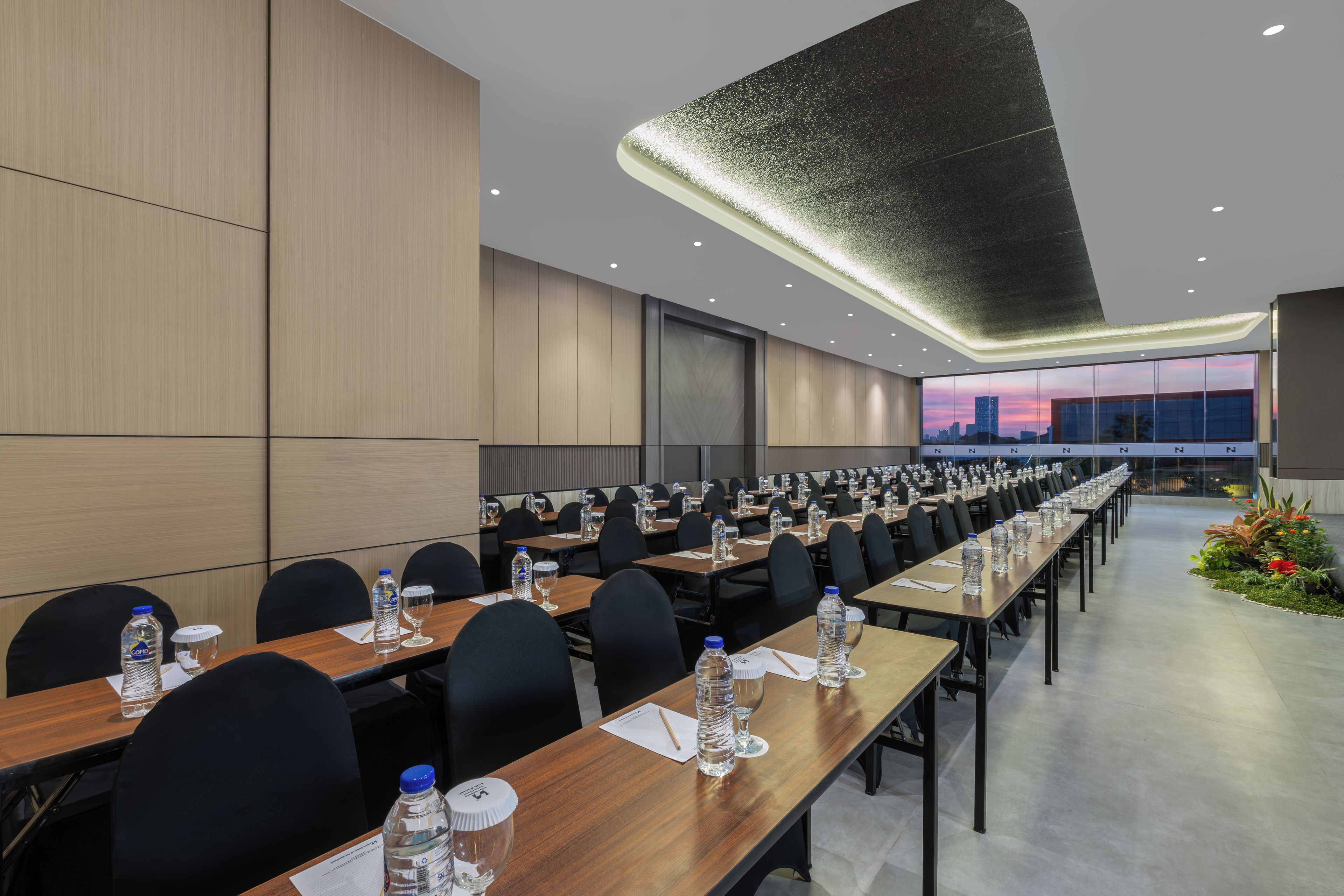 Un salón de conferencias con largas mesas, sillas, botellas de agua y vasos.