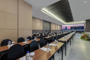 Un salón de conferencias con largas mesas, sillas, botellas de agua y vasos.
