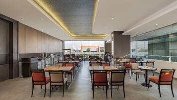 A modern restaurant with a long counter, multiple tables, and chairs.
