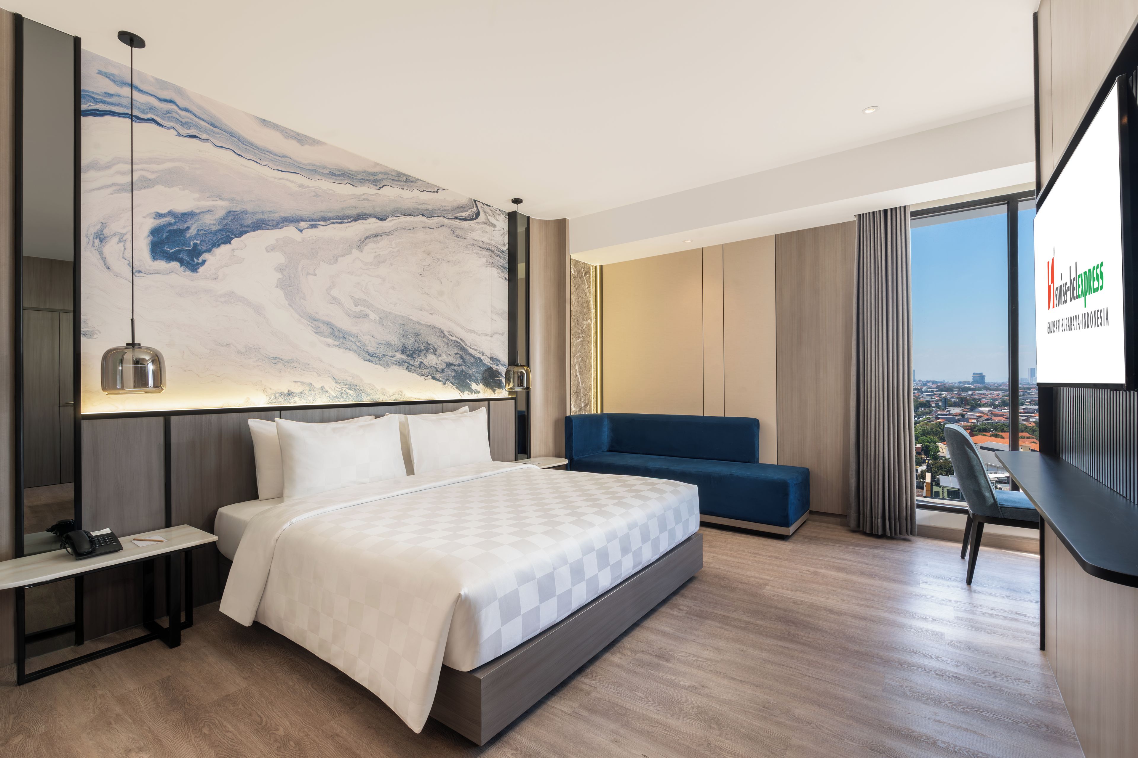 Quarto de hotel moderno com uma cama grande, uma escrivaninha, um sofá azul e vista para a cidade.