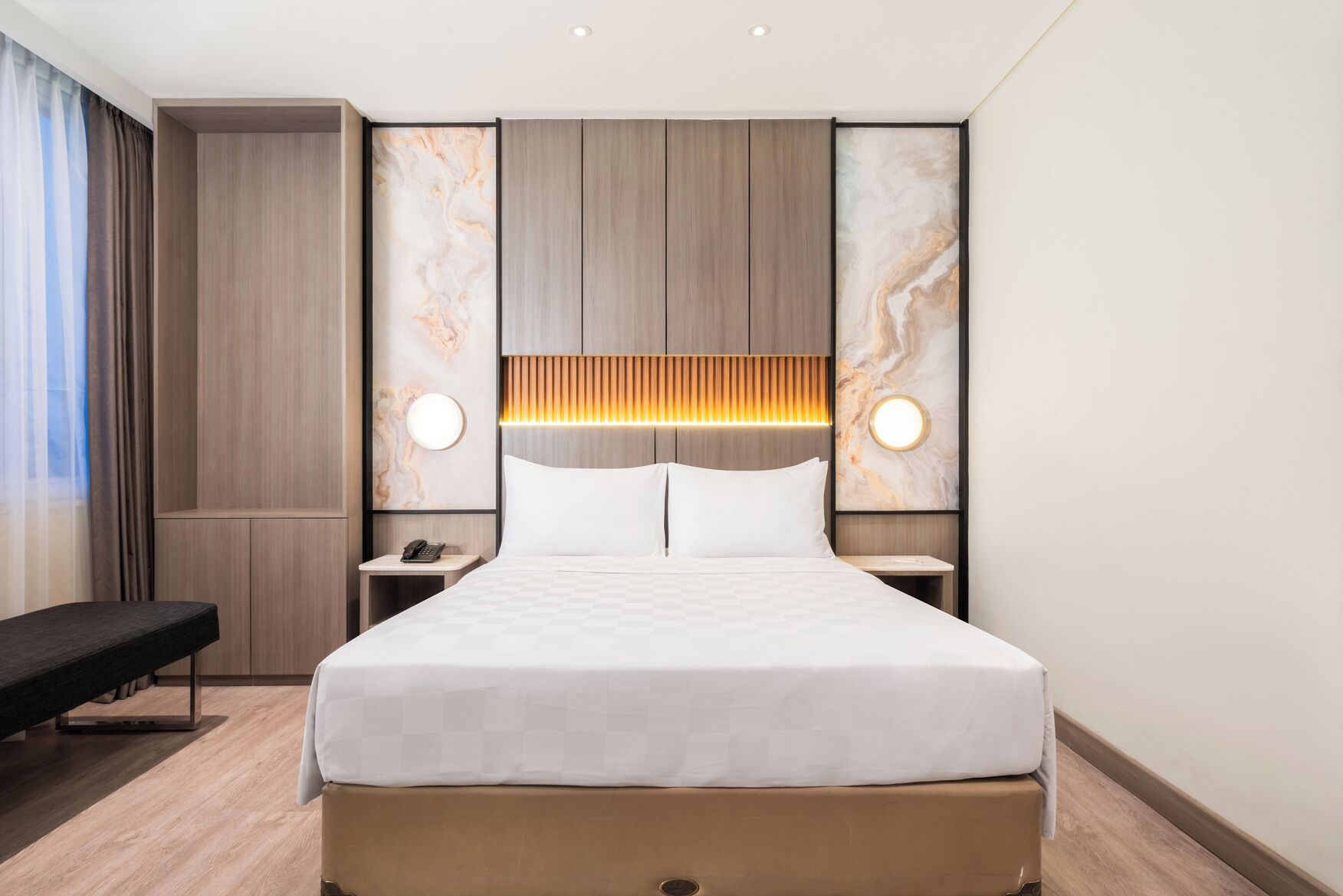 A modern hotel room with a large bed, bedside tables, a bench, and marble wall art.