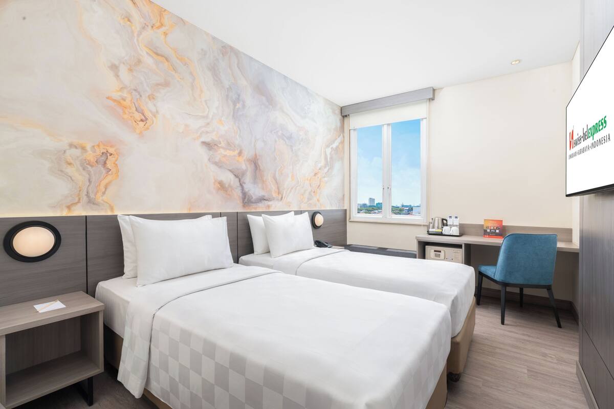 A hotel room with two beds, a desk, a chair, a TV, and a city view.