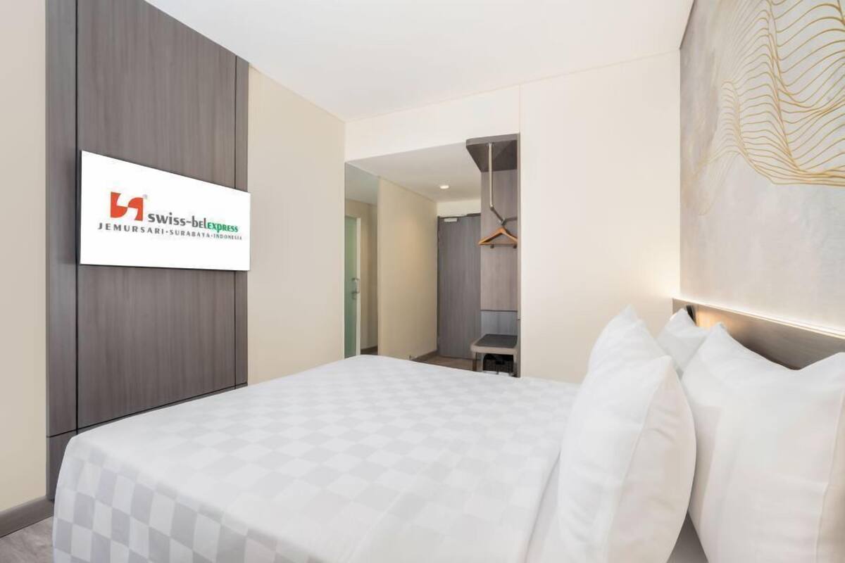 A hotel room with a bed, a mounted TV displaying the hotel name, and a modern interior design.