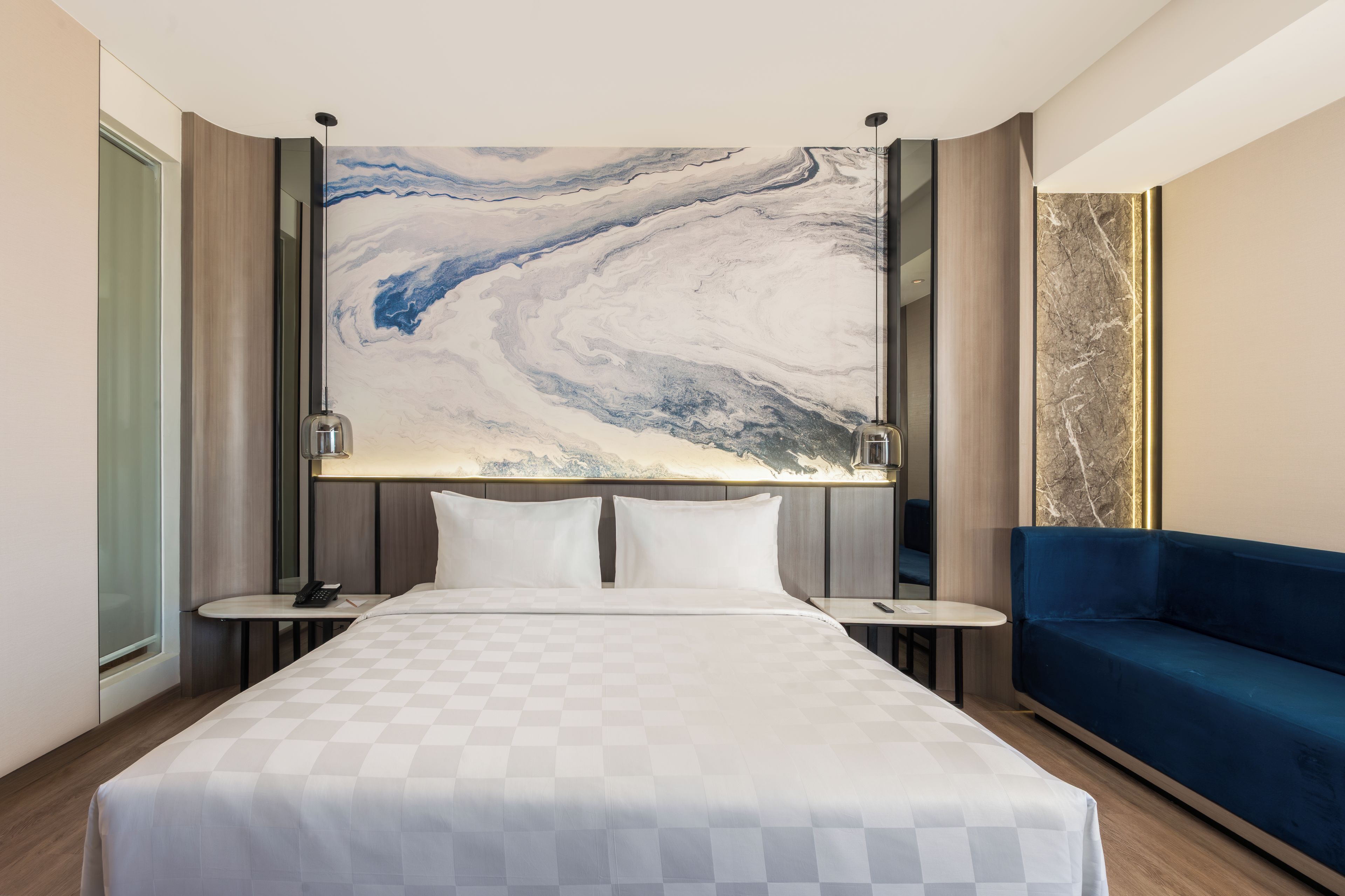 Een hotelkamer met een groot bed, een blauwe bank, marmeren wanddecoratie en een nachtkastje met een telefoon.