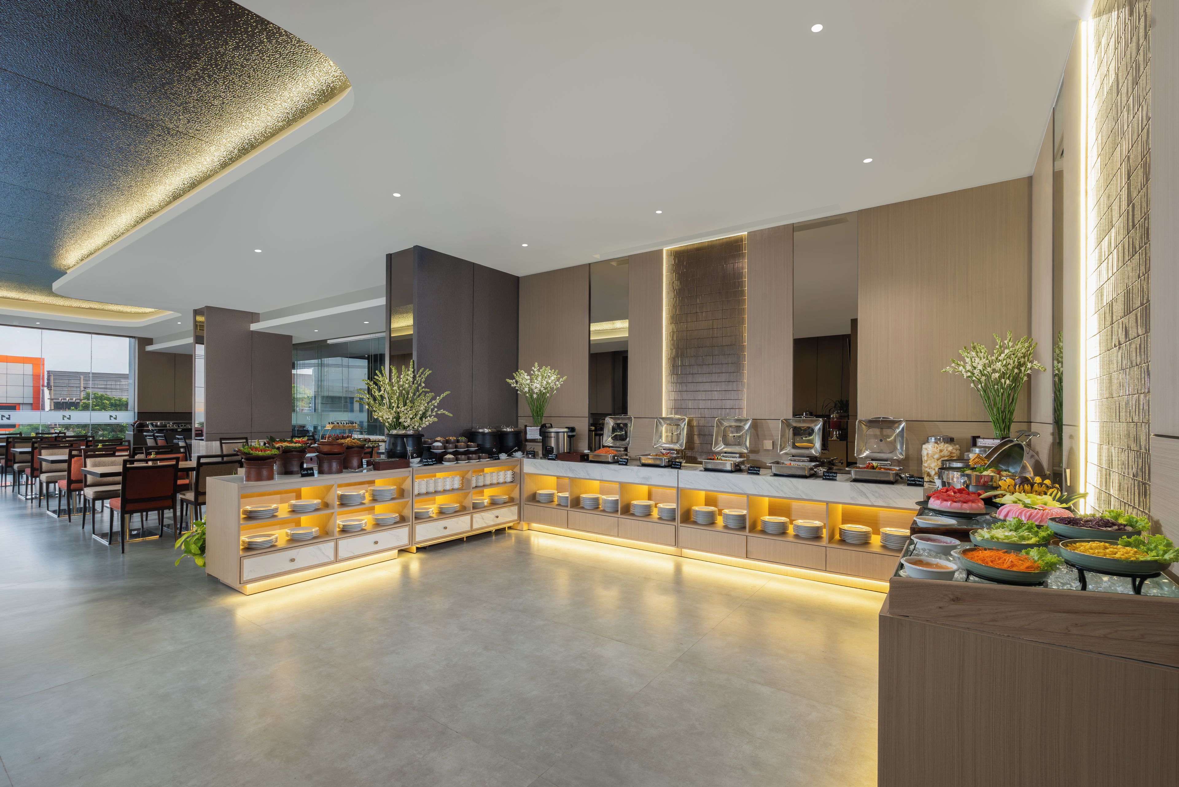 A modern hotel lobby with a central buffet area, seating arrangements, and a view of the outside.