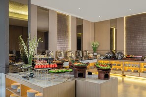 Un moderno vestíbulo de hotel con un área de bufé que presenta distintas estaciones de comida y un espacio de asientos con una decoración floral.