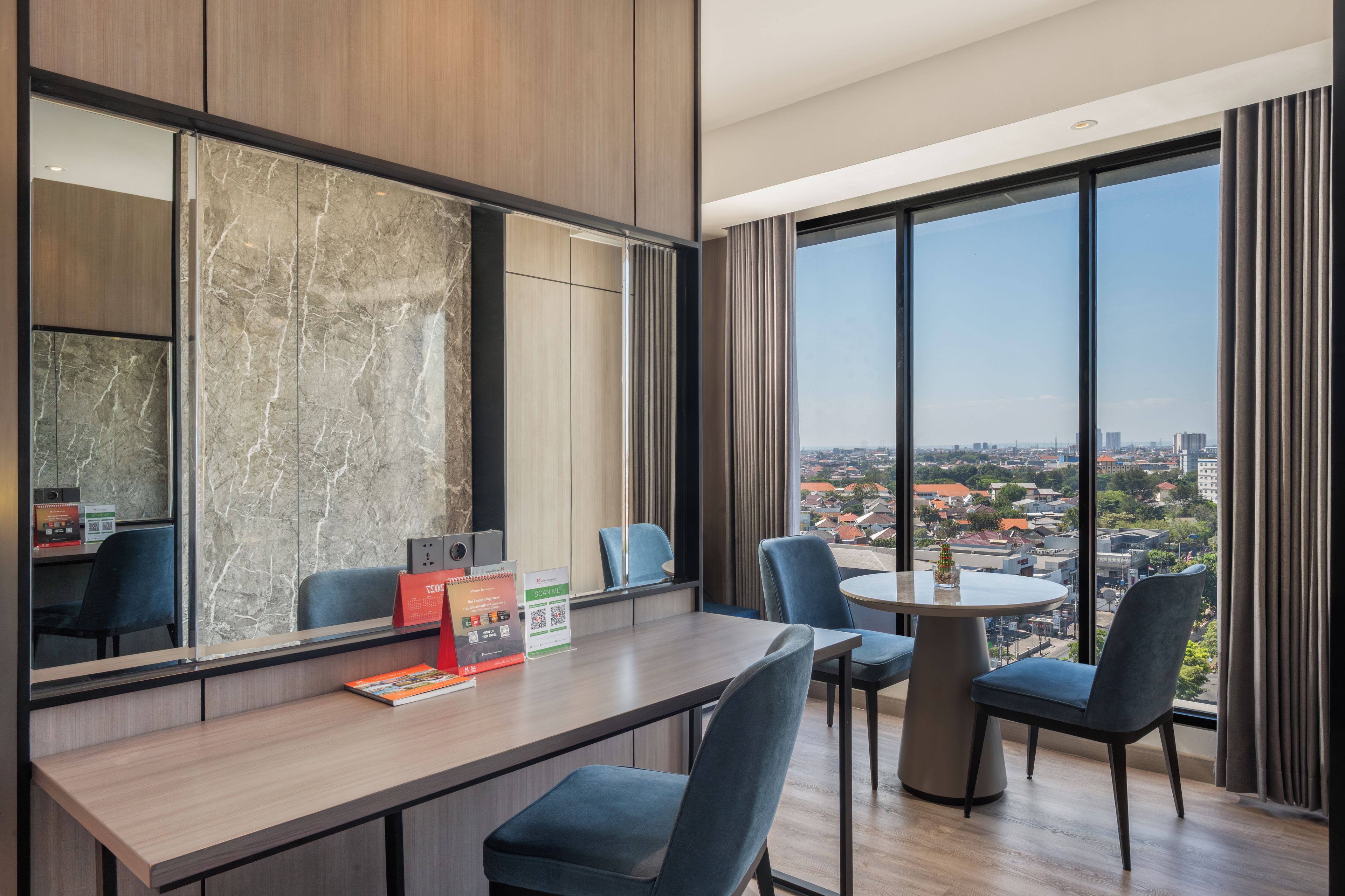 A modern hotel room with a large window, a round table, and a seating area.