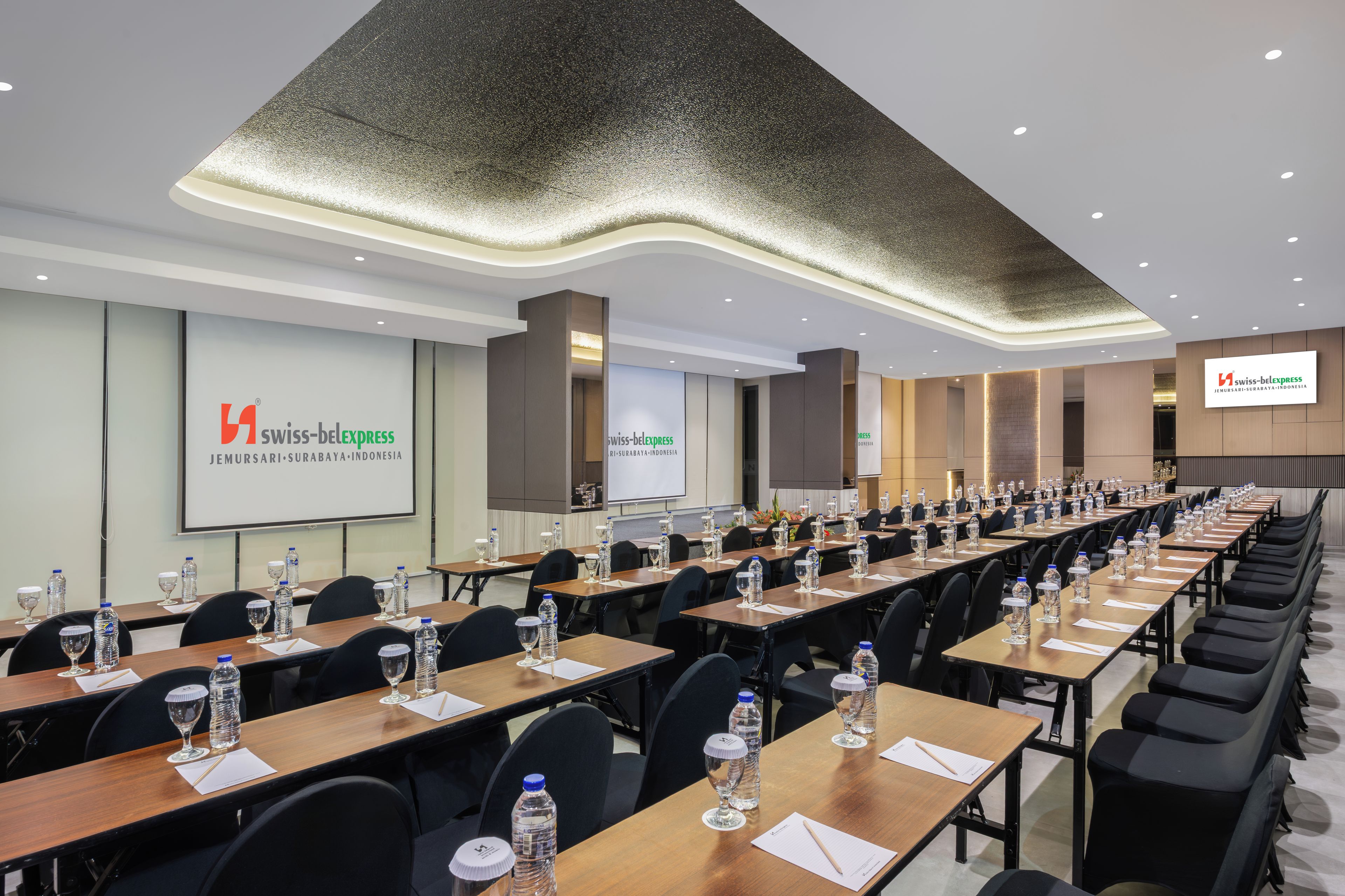 A conference room with long tables, water bottles, and glasses, equipped with a projector screen displaying the Swiss-Belexpress logo.