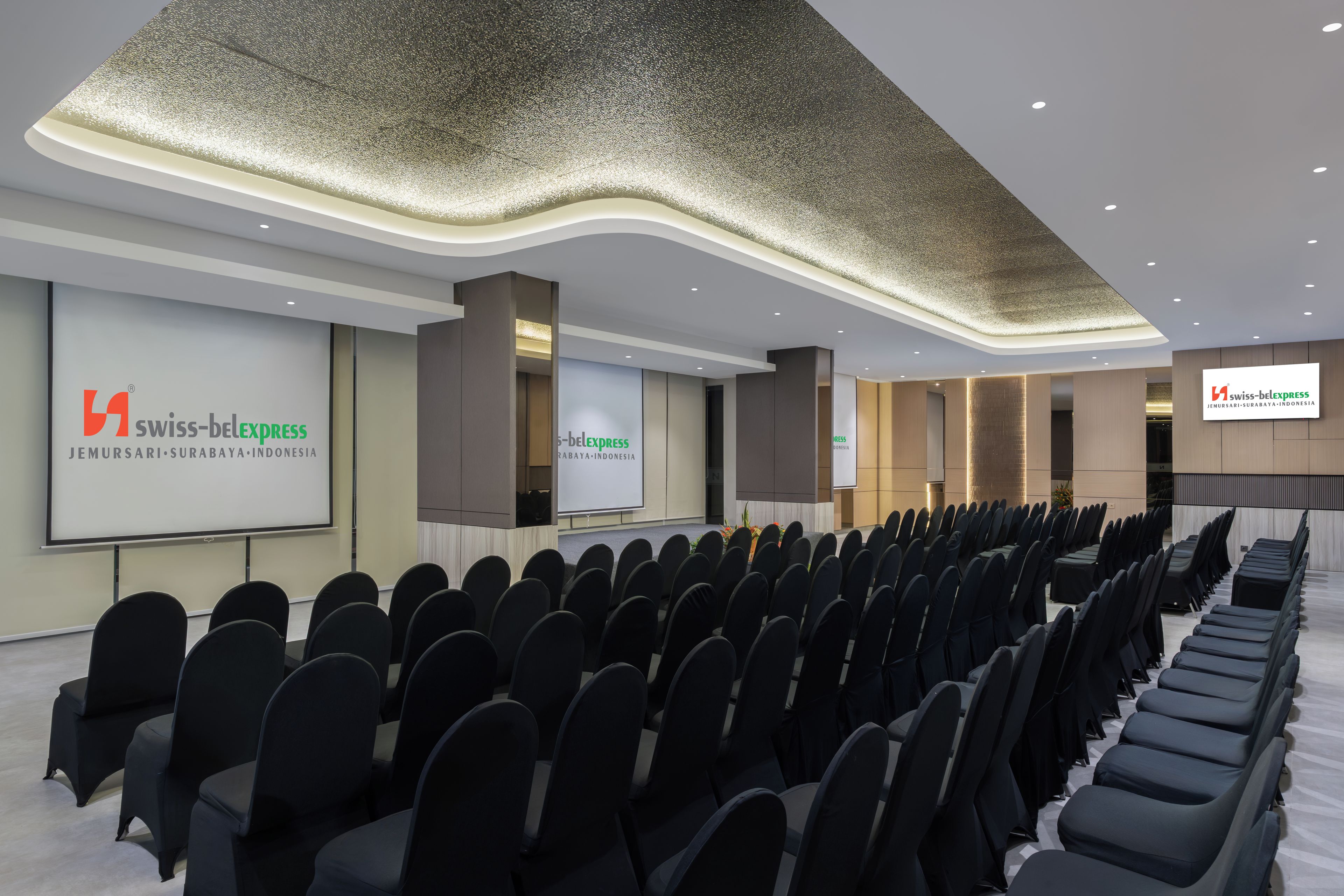 A conference room with rows of chairs, a projection screen, and a modern ceiling design.