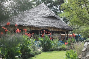 A thatched-roof hut surrounded by lush greenery and vibrant red flowers.