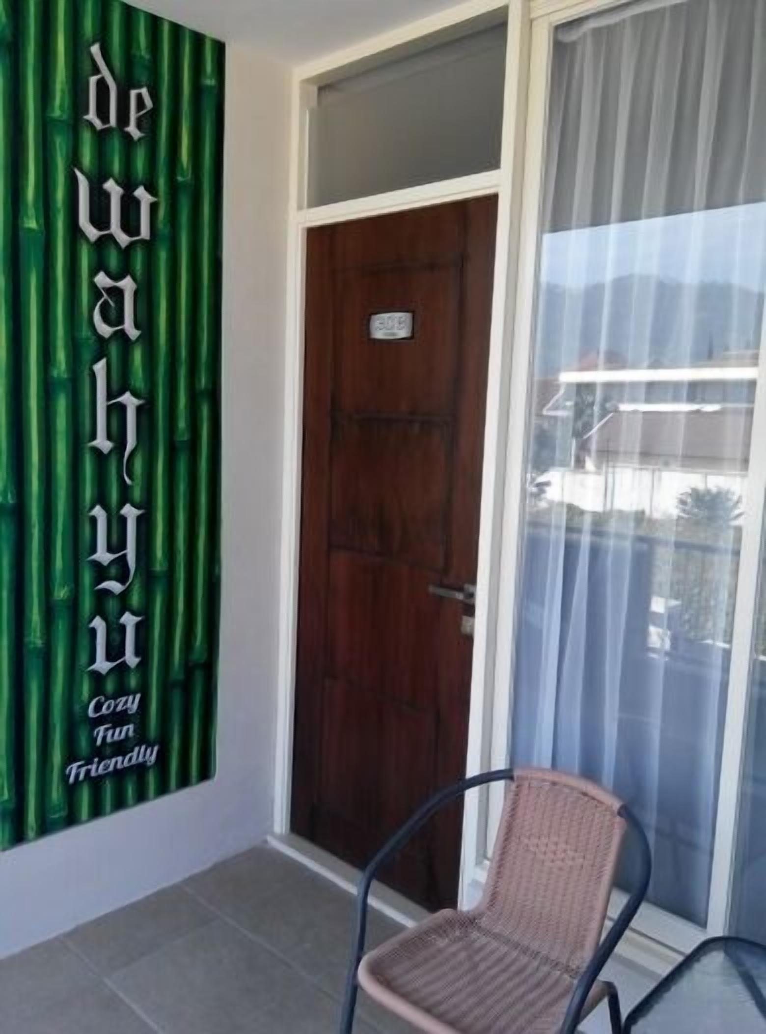 Een kamer met een houten deur, een rieten stoel en een groen paneel met tekst.