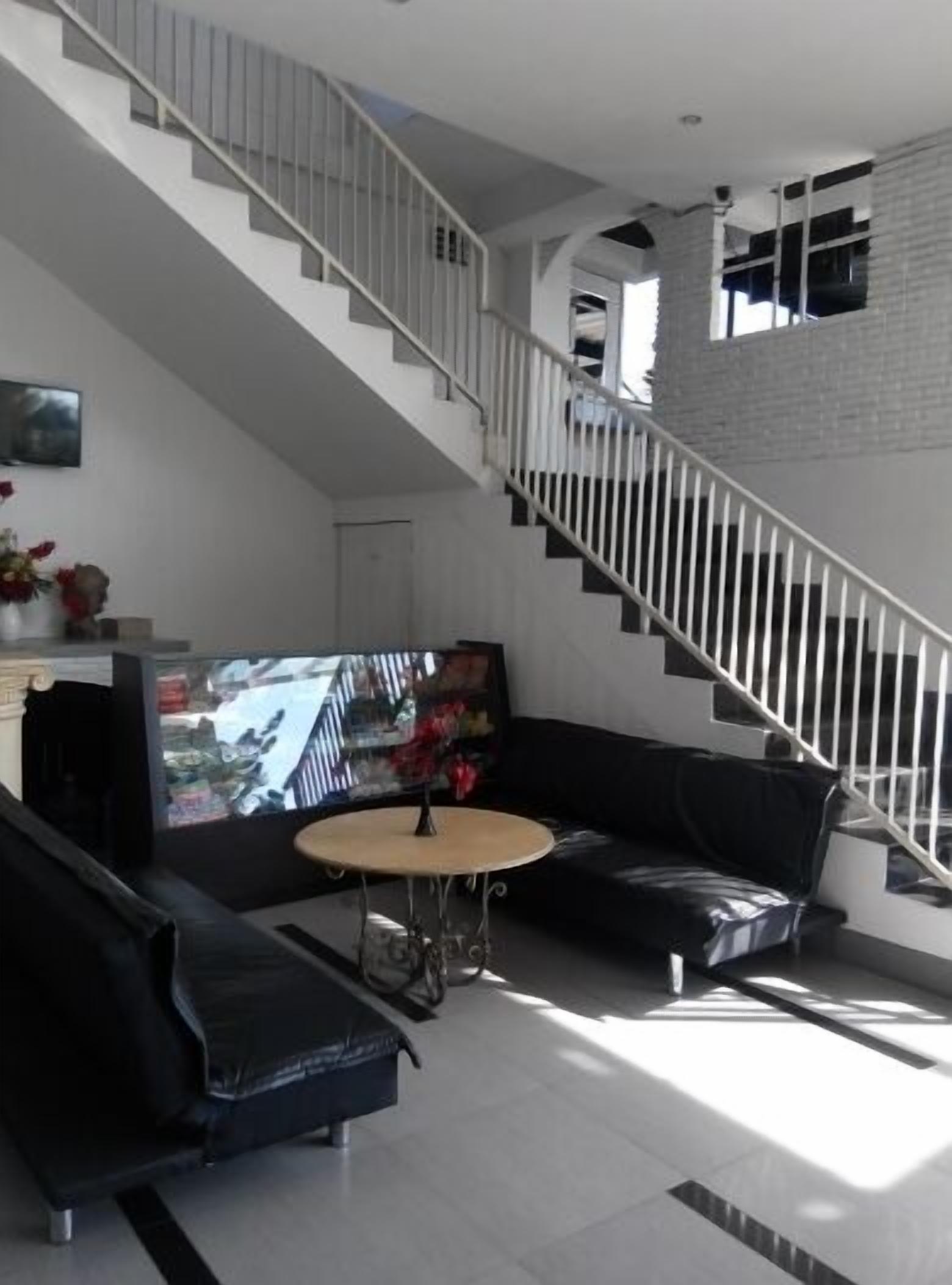 A modern living room with a black leather sofa, a round coffee table, and a staircase with white railings.