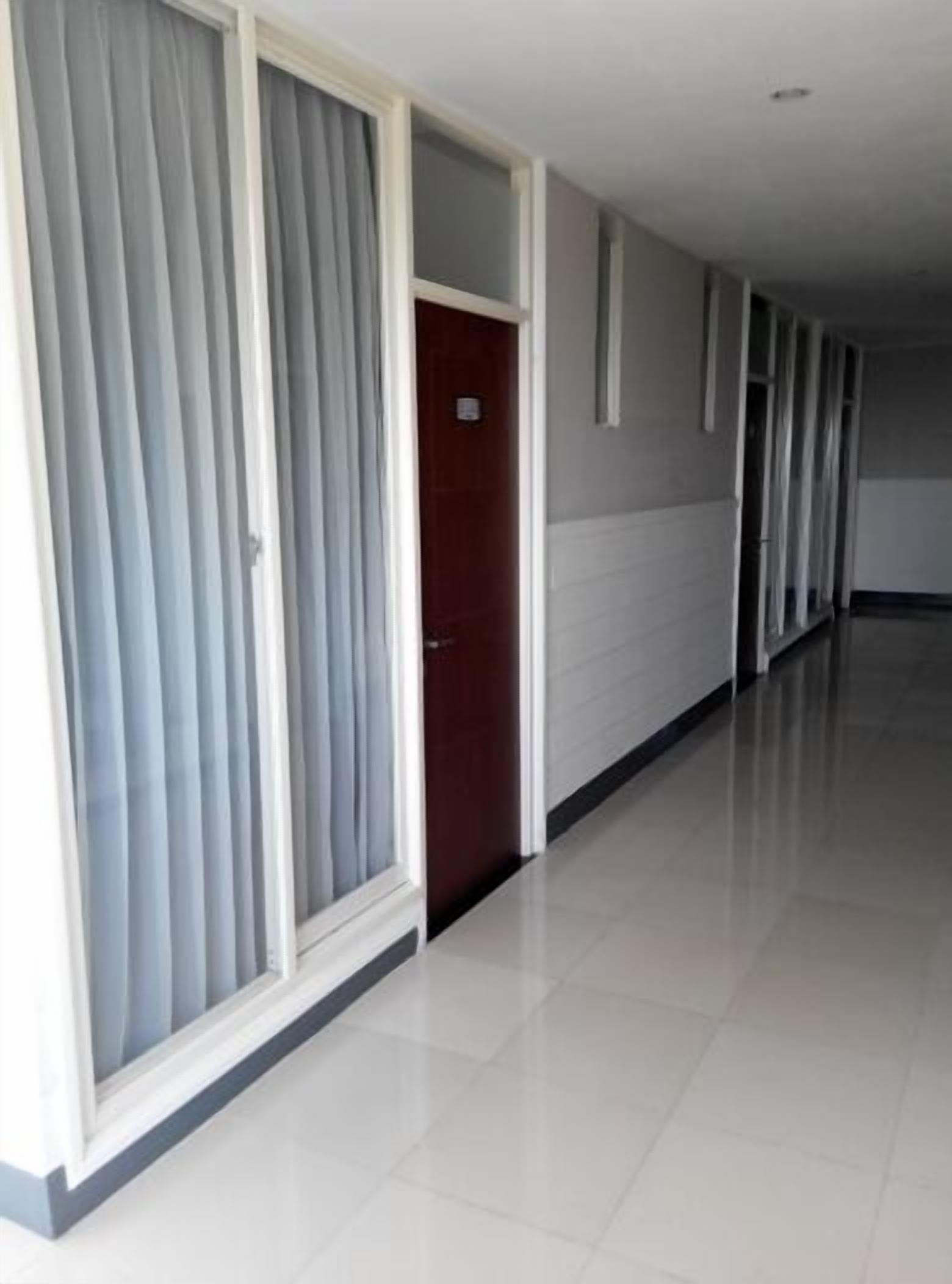 A long, narrow hallway with a wooden door at the end, white walls, and a tiled floor.