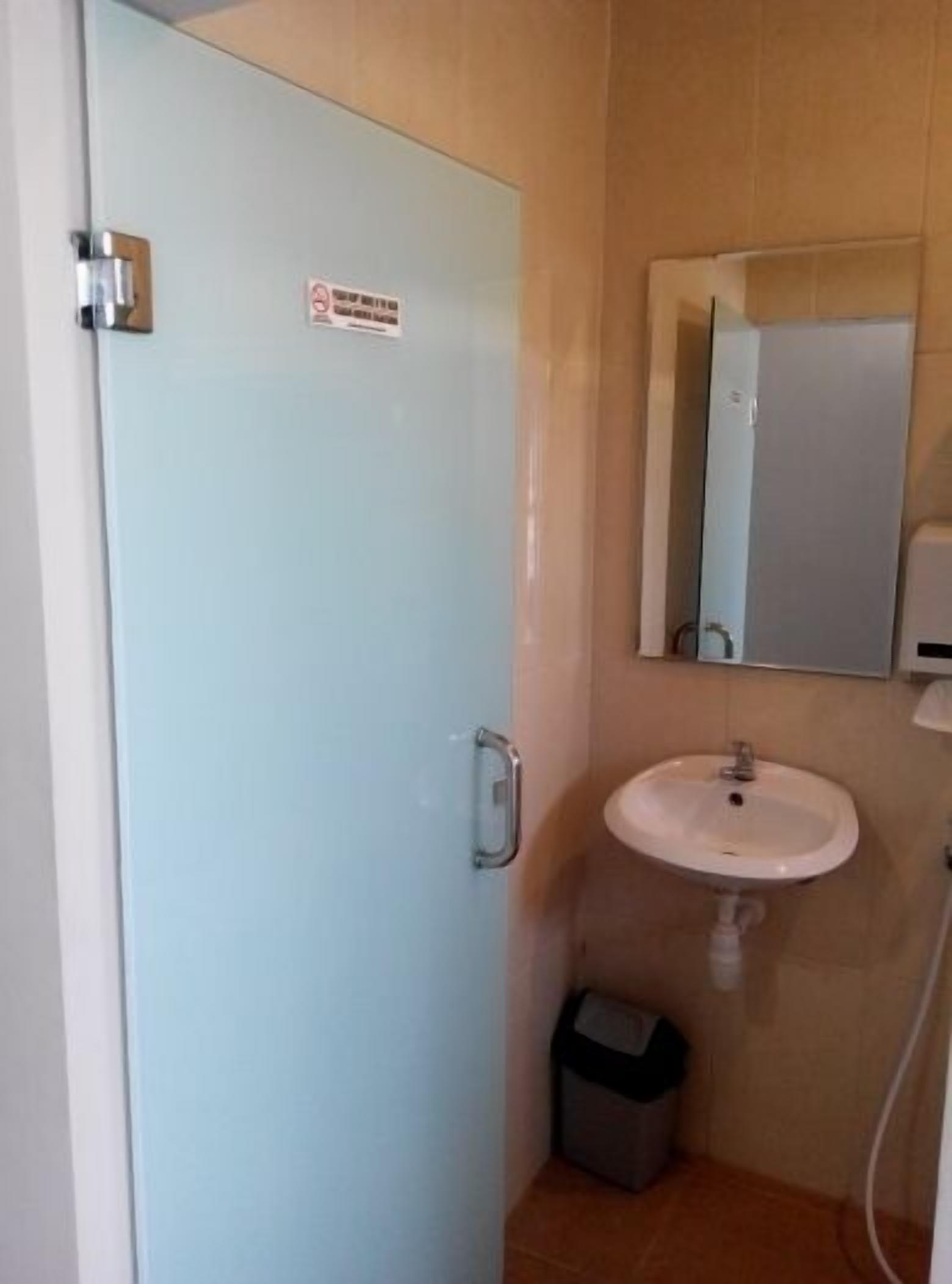 A bathroom with a light blue door, a white sink, a mirror, and a trash bin.