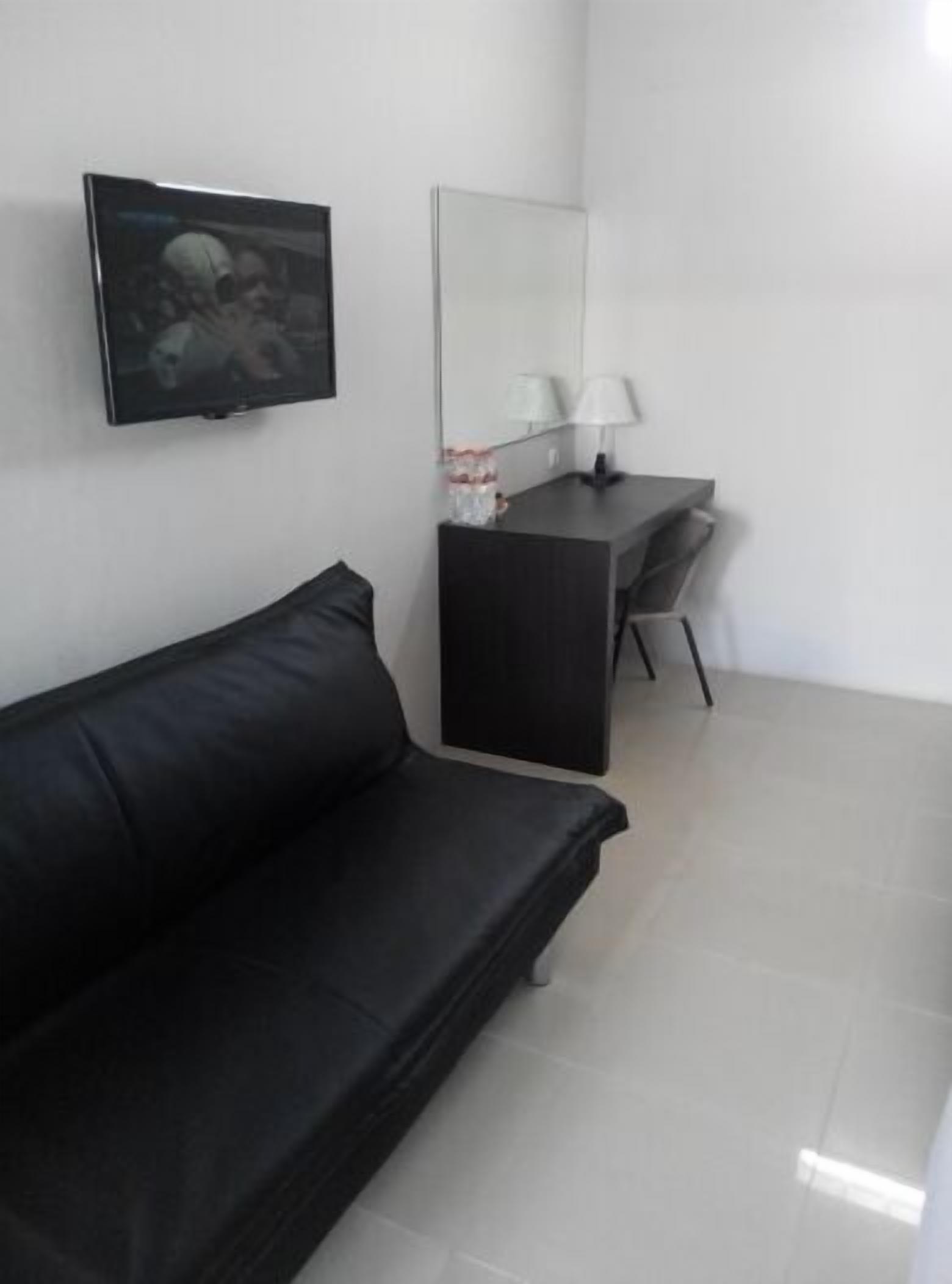 A modern room with a black leather sofa, a desk with a lamp, and a TV mounted on the wall.