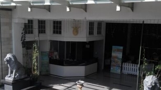 Un patio con dos estatuas de leones, una fuente central y la entrada de un edificio con puerta de vidrio.