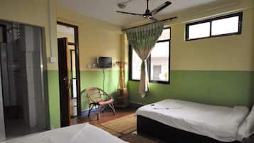 A room with two beds, a ceiling fan, a television, and a window with curtains.