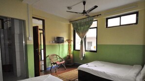 A room with two beds, a ceiling fan, a television, a chair, and a window with curtains. - Metro Eco Hotel (Kathmandu)