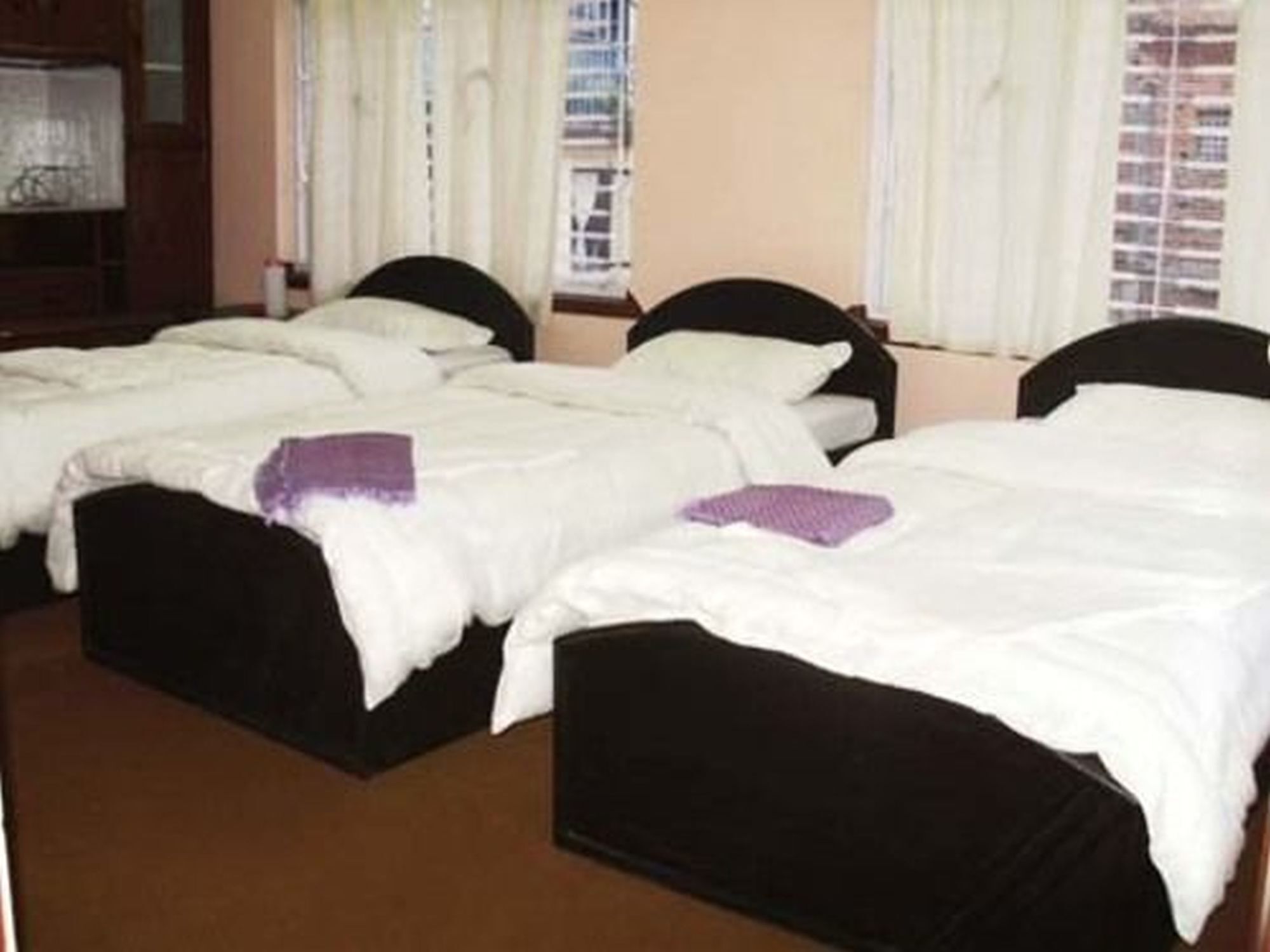 A hotel room with three single beds, each with a black headboard and white bedding.