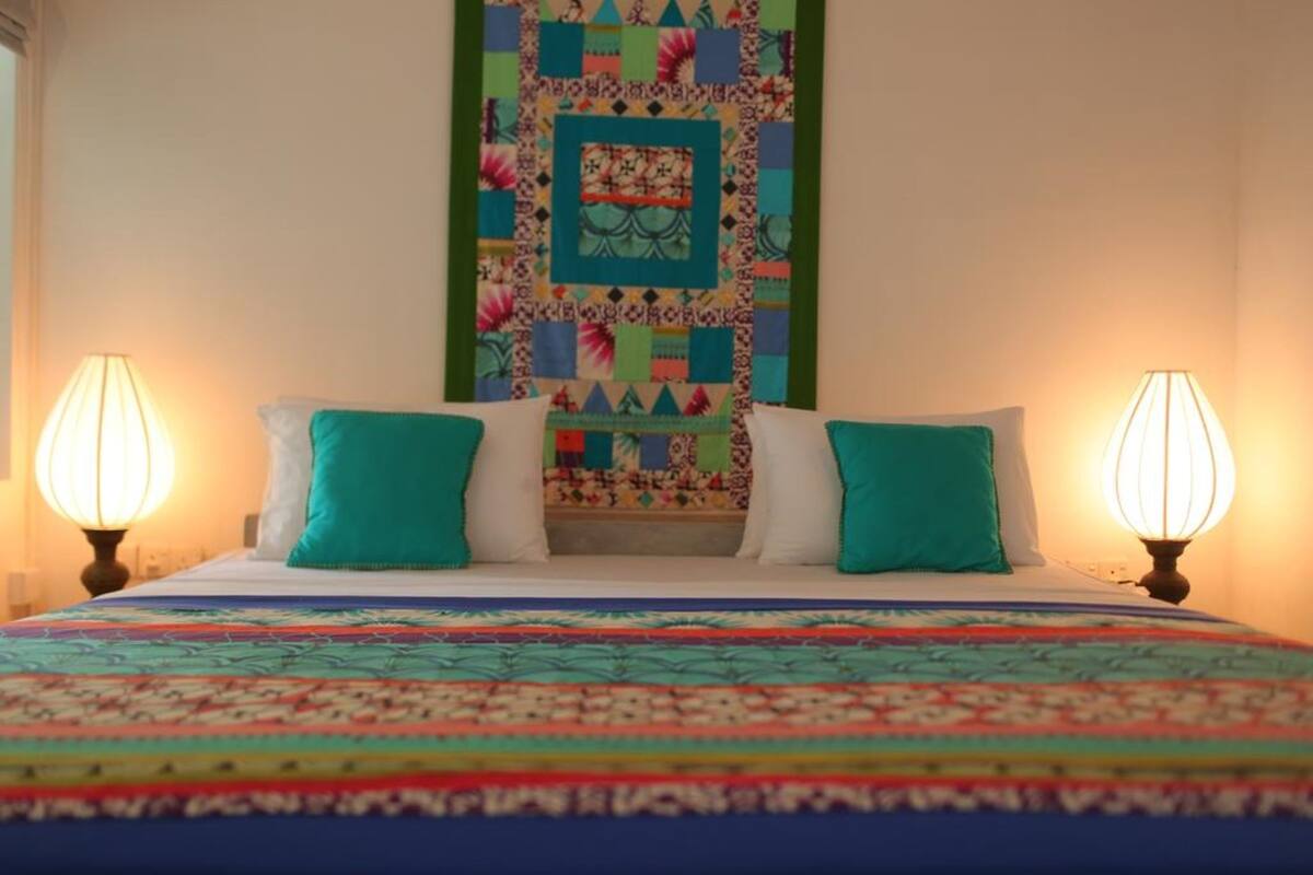 A bed with a colorful quilt, two teal pillows, and two bedside lamps.