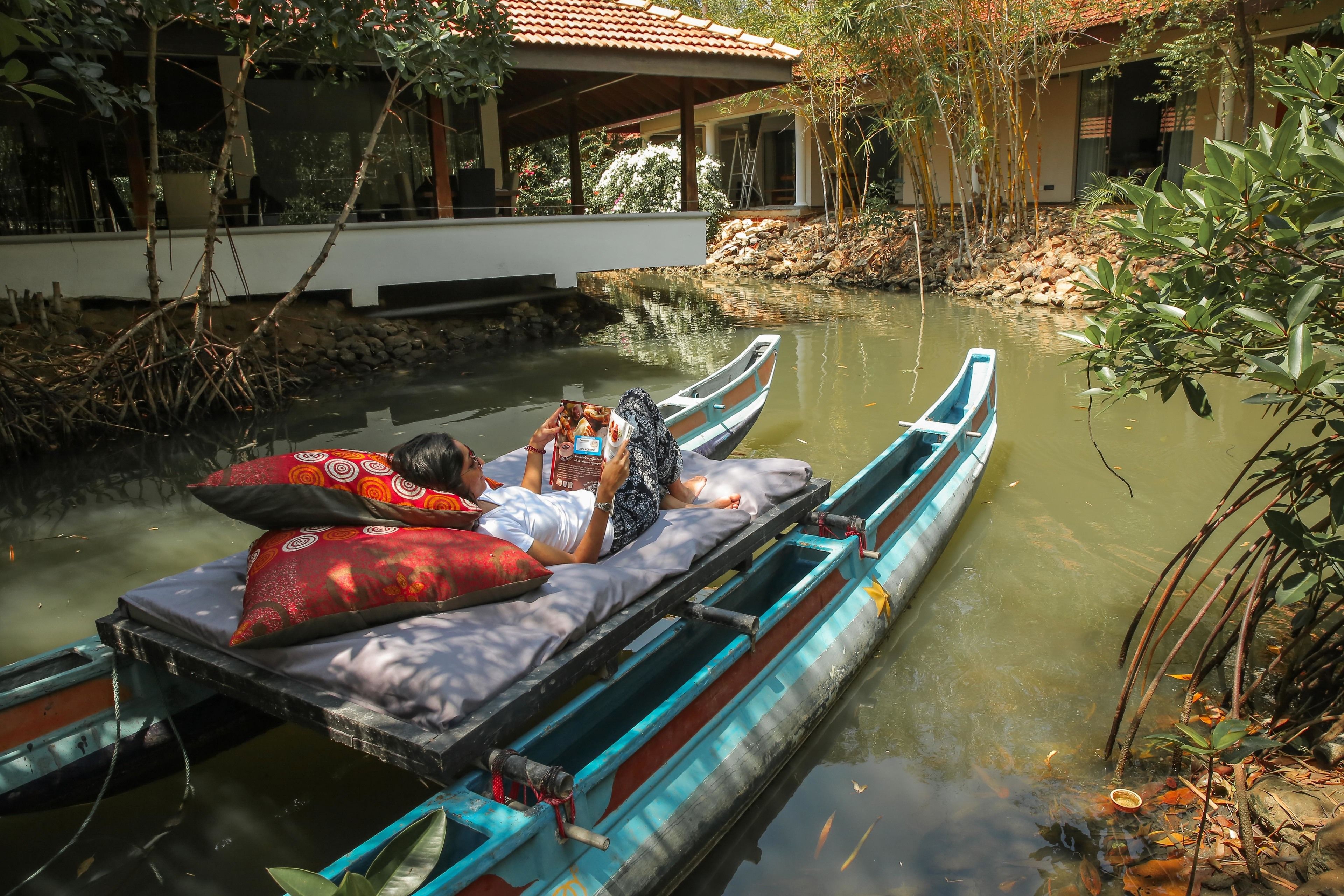 Ein langes, schmales Boot mit zwei Personen, die auf dem Deck liegen, umgeben von Wasser und viel Grün.