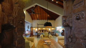 A spacious room with a high ceiling, wooden beams, a large wooden table, and a bed with a colorful headboard. - Villa Hundira (Negombo)