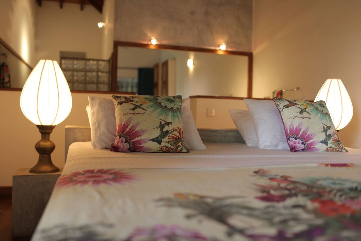 A hotel room with a bed, two bedside lamps, and floral-patterned pillows.