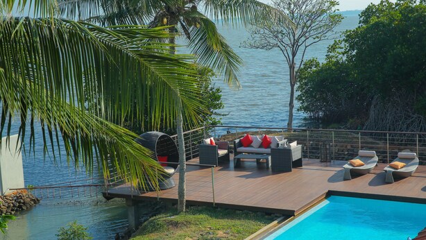 A poolside area with outdoor furniture, a view of the sea, and a wooden deck. - Villa Hundira (Negombo)