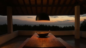 A wooden table with a bowl under a hanging lamp, overlooking a sunset view. - Villa Hundira (Negombo)