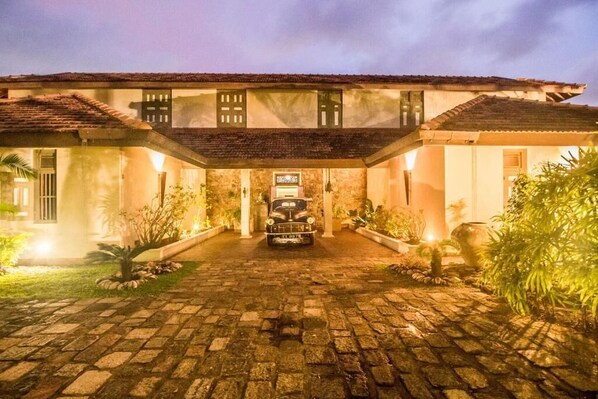 A two-story building with a cobblestone driveway leading to a car parked in front. - Villa Hundira (Negombo)