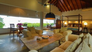 A spacious living area with a wooden coffee table, comfortable seating, a large window with a view, and a ceiling fan. - Villa Hundira (Negombo)
