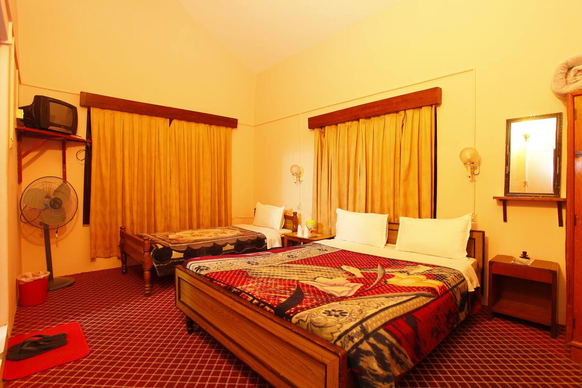 A hotel room with two beds, a fan, a television, and a mirror.