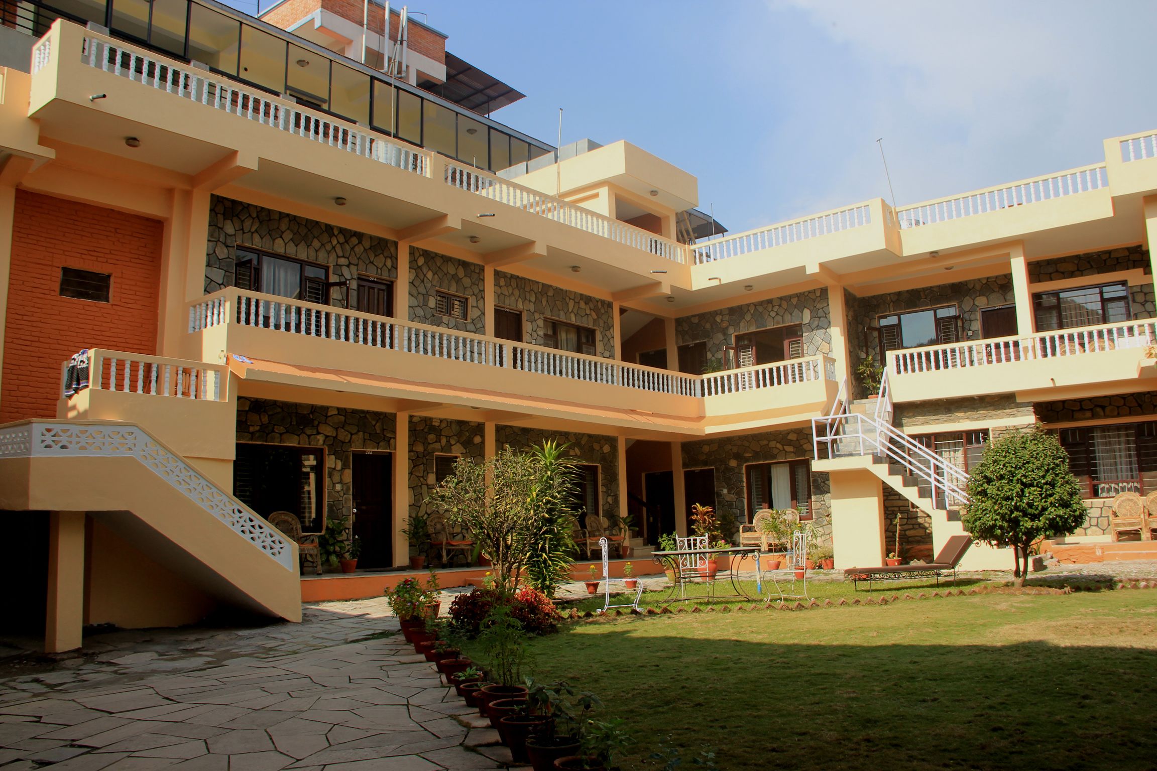 A multi-story building with balconies, a staircase, and a garden area with potted plants.