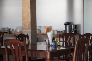 Een eettafel met houten stoelen, een granieten pilaar en diverse toevoegingen en een koffiezetapparaat op tafel.