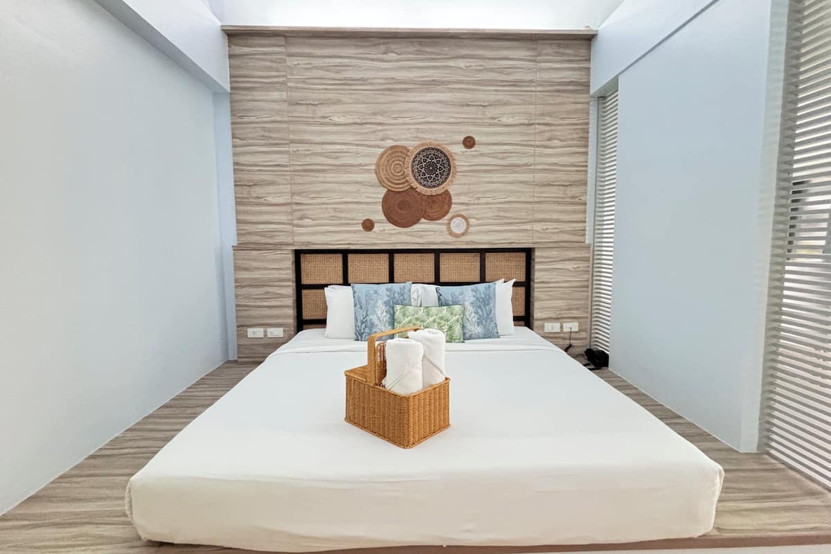 Quarto de hotel moderno com uma cama grande, uma parede de destaque em madeira e um adorno pendurado na parede.