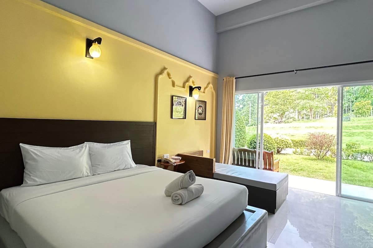 Quarto de hotel moderno com uma cama grande, mesa de cabeceira, uma cadeira e vista para o exterior.