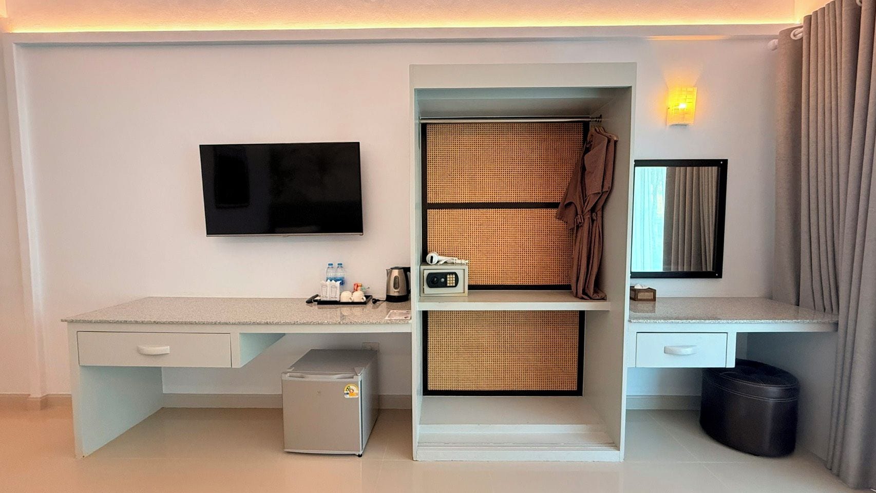 Una camera d'albergo compatta con un letto, una scrivania con televisione a schermo piatto, un piccolo frigorifero e un angolo bagno.