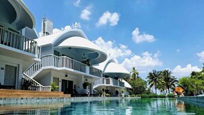 Un resort moderno con una piscina grande, varios balcones y un cielo azul despejado.