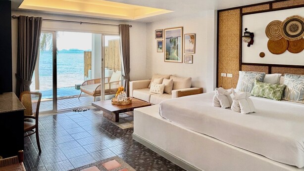 Une chambre d’hôtel avec un grand lit, un canapé, une table à manger et une vue sur la mer.