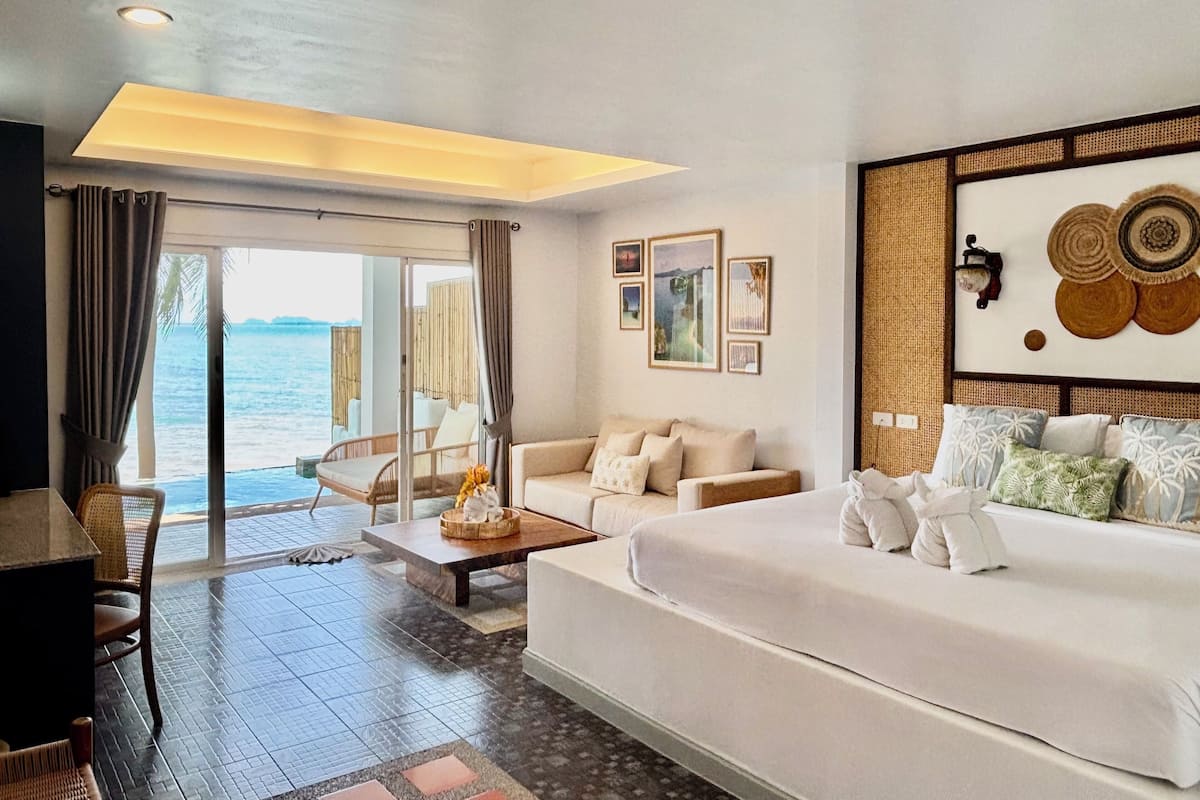 Quarto de hotel com uma cama grande, um sofá, uma mesa de jantar e vista para o mar.