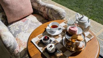 Una mesa redonda de madera con un juego de té, que incluye una tetera, tazas y platitos, y una bandeja con pasteles y un pequeño bol de mermelada.