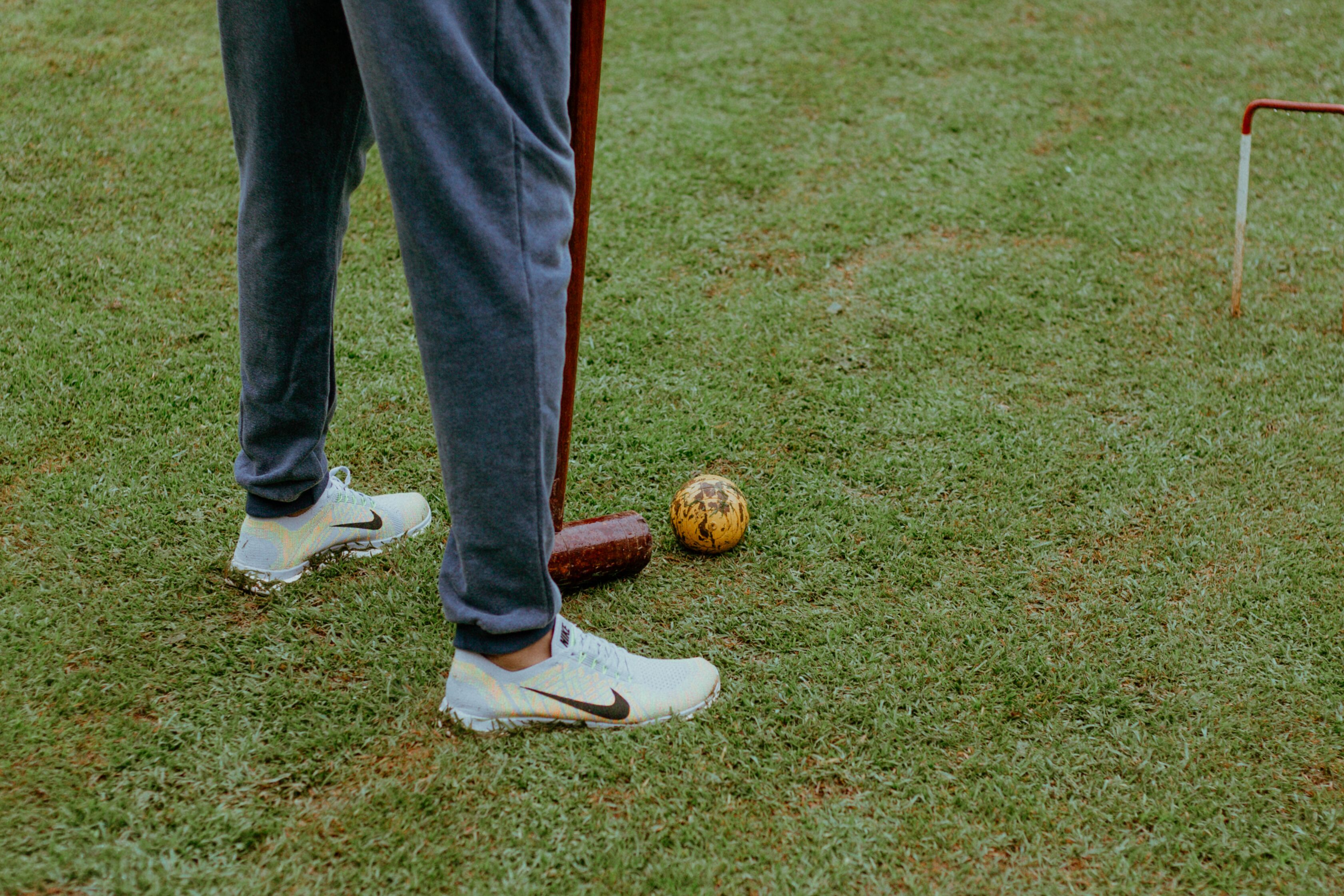 A person standing on grass with a croquet ball and mallet.