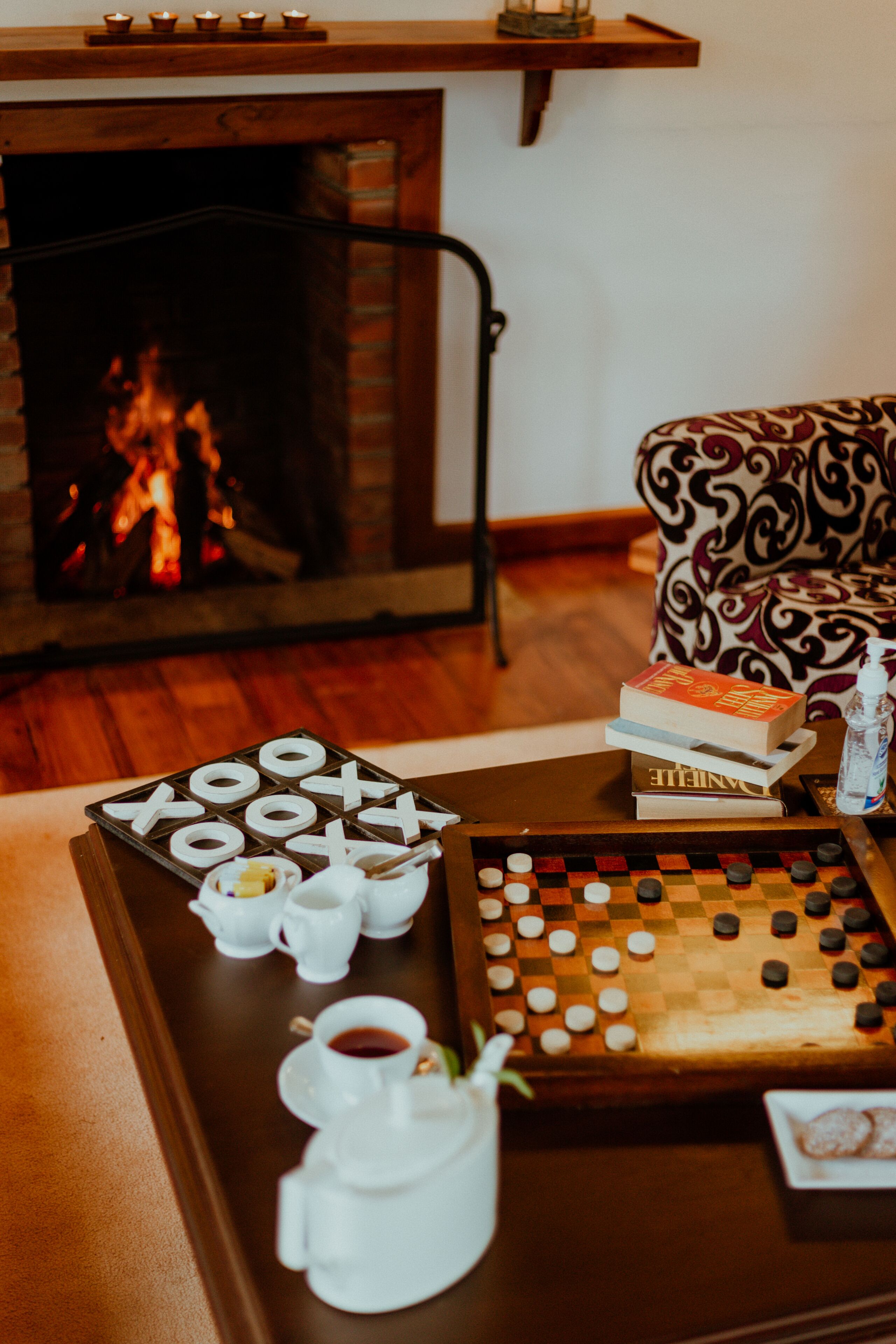 A cozy room with a fireplace, a checkered board game, books, and a tray with cups and a teapot.